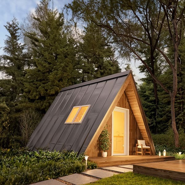 A compact wooden A-frame cabin with a dark metal roof and warm interior lighting stands in a lush garden setting at twilight.