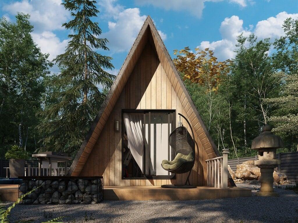 A modern wooden A-frame cabin nestled in a lush forest, featuring a cozy front deck with a hanging egg chair.